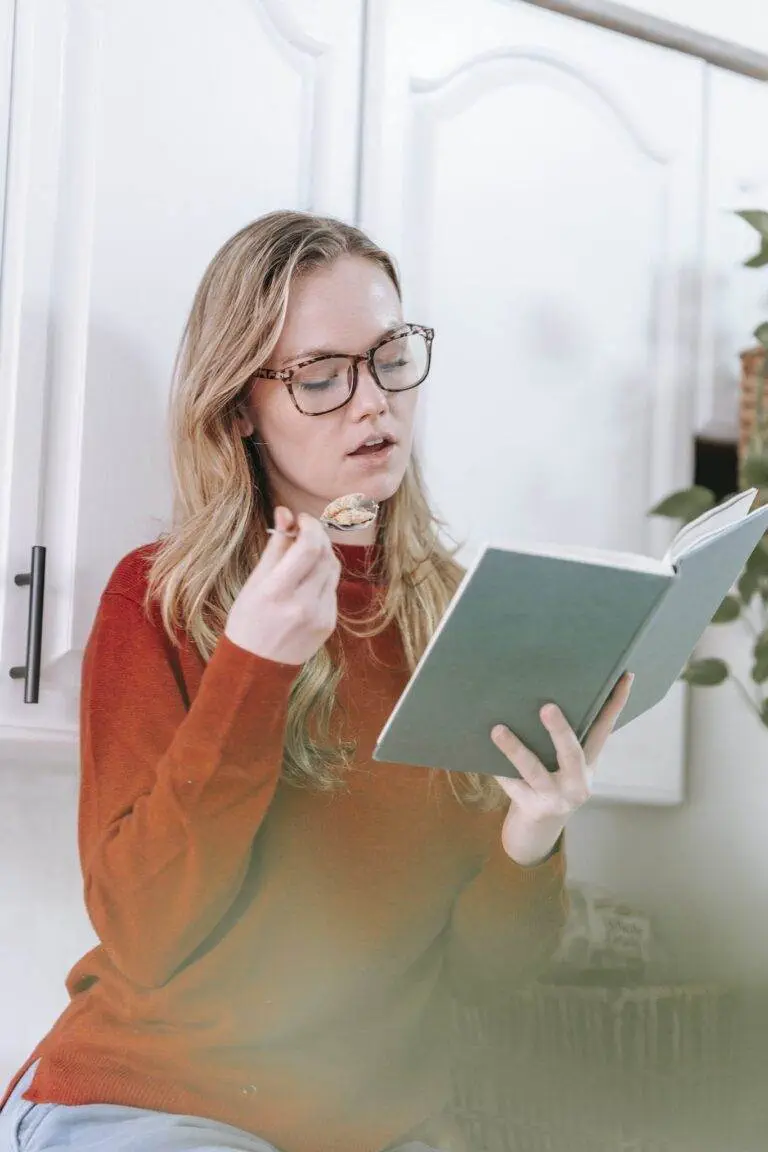 Attentive young lady reading book during breakfast in kitchen
